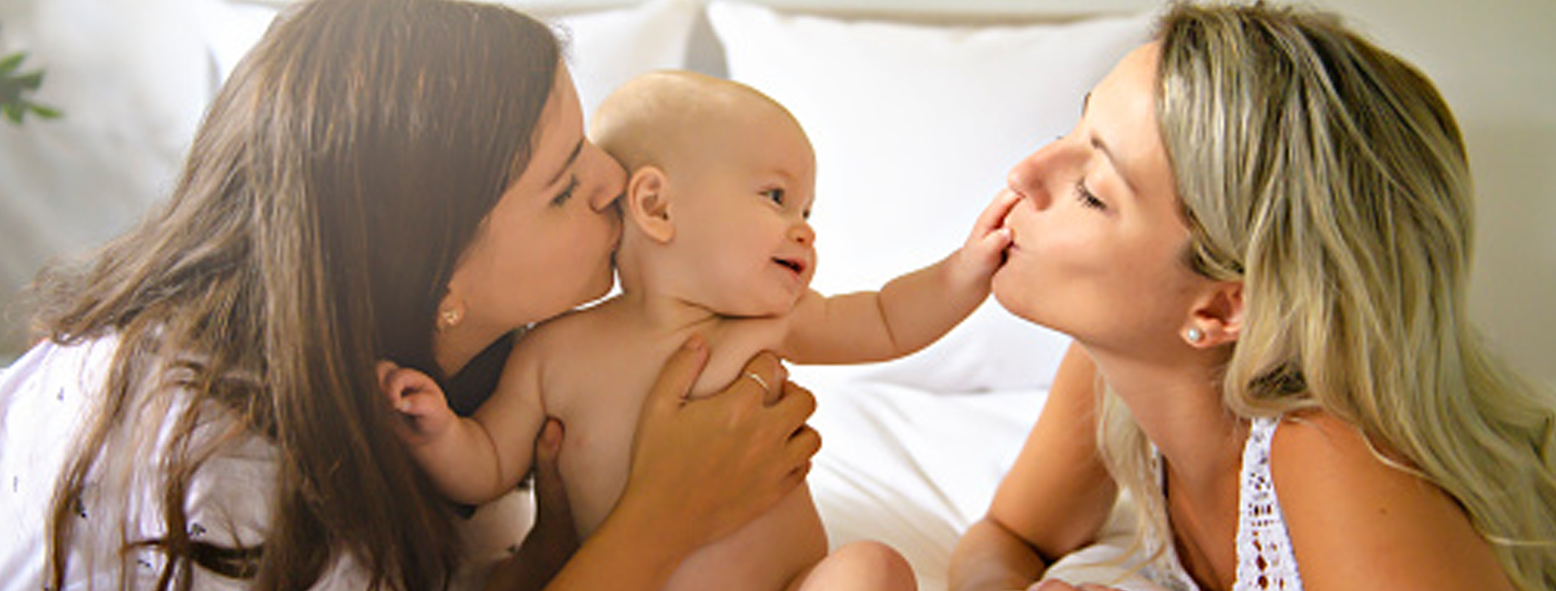 Image of a baby being kissed and hugged by two female family members.